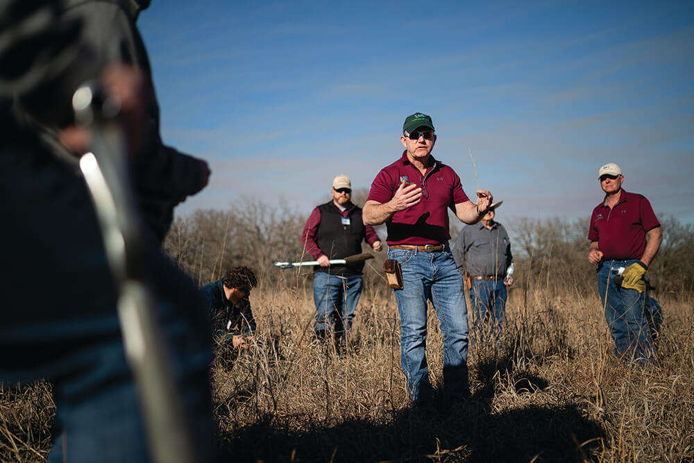 Allen Williams, Ph.D. and Noble employees stand in a pasture on Noble campus, holding shovels and discussing regenerative agriculture.